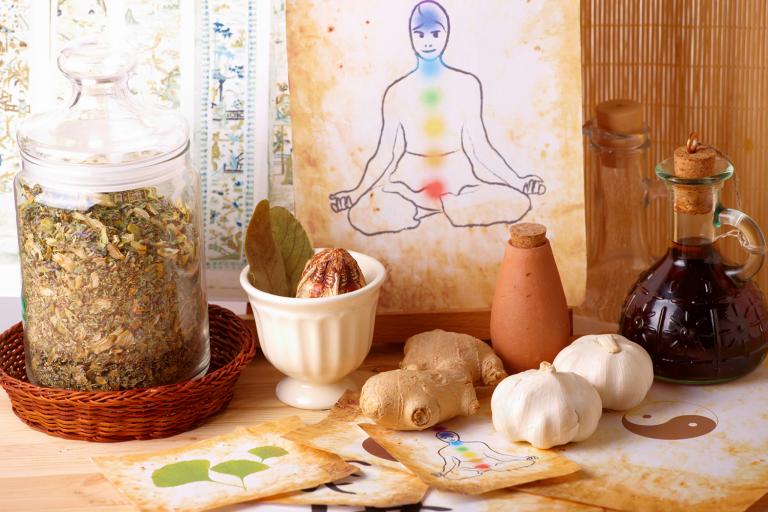 Traditional alternative therapy theme with medicinal herbs and oils with a watercolor of a silhouette of man with chakras in the background.