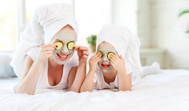Mother and child with natural face masks on, covering eyes with cucumber slices.